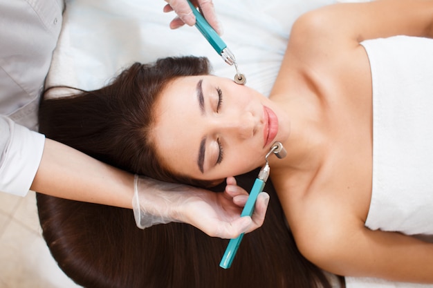 Photo cosmétologie. belle femme à la clinique de spa recevant un traitement facial électrique stimulant du thérapeute.