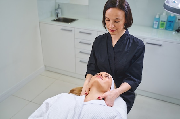 Cosmétologie esthétique. Jolie fille blonde allongée sur le canapé tout en faisant une procédure de beauté dans un salon