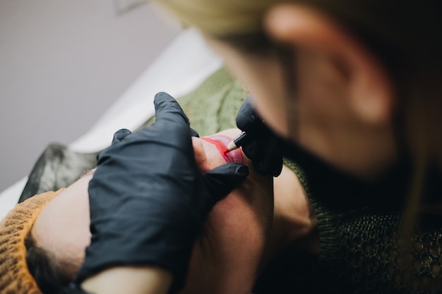 Le cosmétologue applique la couleur pour le maquillage permanent aux lèvres femelles