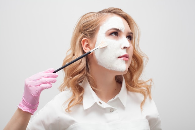 La cosmétologue applique le masque sur le visage avec un pinceau. Concept de soins de la peau du visage.