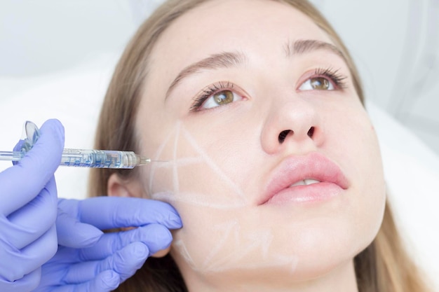 Photo le cosmétologue dessine les contours avec un crayon blanc sur le visage du patient marquage schématique avant de dessiner les contours préparation d'un visage agrandi pour les procédures cosmétiques