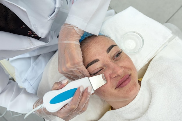 Le cosmétologue effectue une procédure de soins du visage à l'aide d'une spatule à ultrasons pour un client