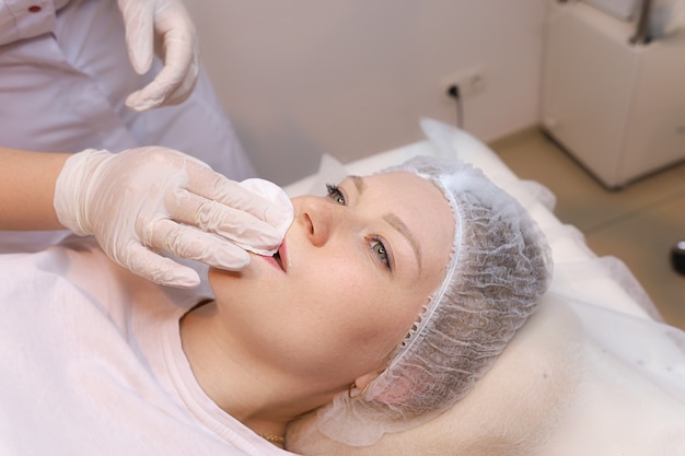 Le cosmétologue essuie les restes d'anesthésie des lèvres du client avec une éponge de coton