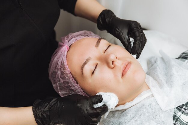 Un cosmétologue fait un massage facial cosmétique pour le visage d'une jeune femme détendue dans un spa de beauté Soins du visage massage soins de la peau concept de cosmétologie