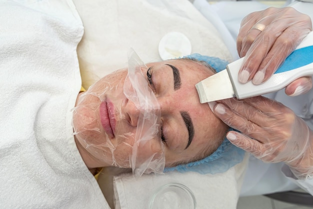 Le cosmétologue en gants de latex applique un masque rajeunissant sur le visage d'une femme avec une spatule