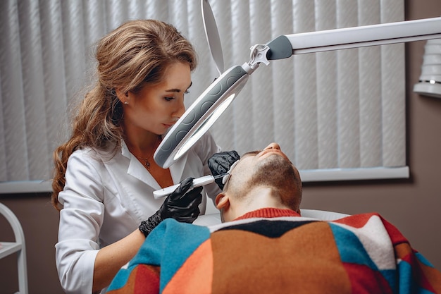 Un cosmétologue nettoie la peau d'un homme avec une machine à ultrasons moderne dans le bureau du salon de beauté