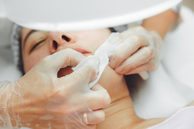 Un cosmétologue nettoie le visage sous une loupe cosmétique Le concept de cosmétologie Un cosmétologue effectue une procédure de nettoyage du visage avec une peau à problèmes