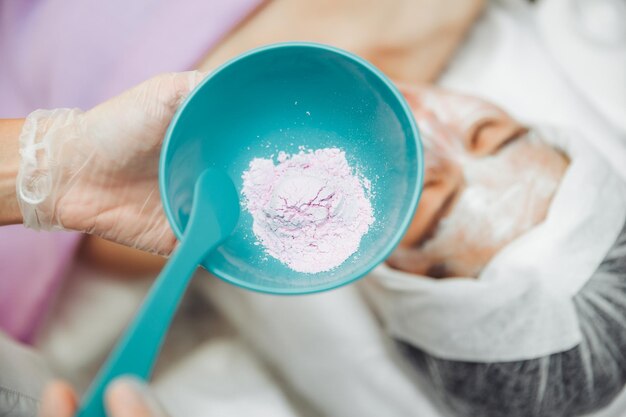 Photo un cosmétologue prépare un masque d'alginate lilas à minsk masque d'alginate pour la peau cosmétologie procédure de soins de la peau cosmétologue prépare un masque rajeunissant