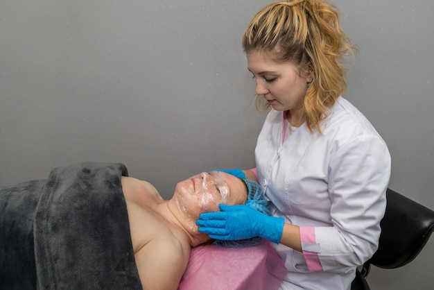 Un cosmétologue professionnel couvre le visage d'une femme adulte avec un film de polyéthylène Concept pour les soins de la peau dans un salon de spa