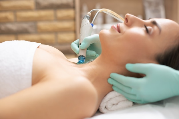 Cosmétologue professionnel effectuant la procédure de dermabrasion sur la peau d'un jeune client satisfait