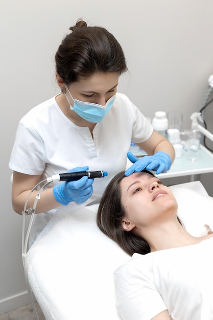 Cosmétologue qualifié intelligent utilisant un appareil moderne tout en faisant une procédure hydrafaciale