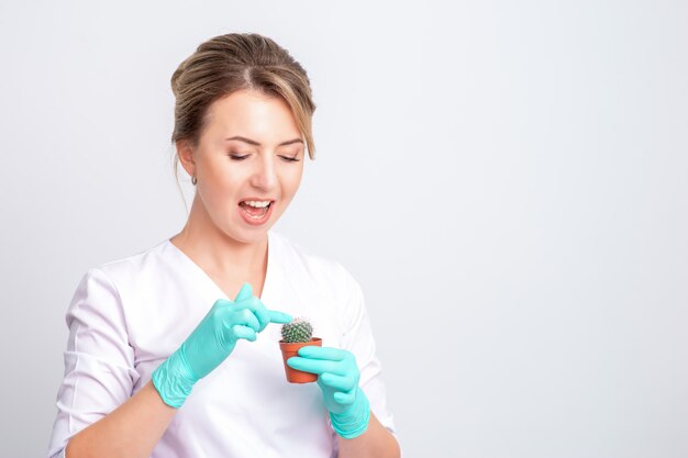 Cosmétologue tient un cactus vert dans un pot brun sur blanc.