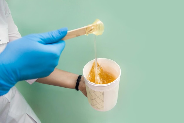 Le cosmétologue tient un pot de cire de sucre montre la texture de la pâte avec une spatule