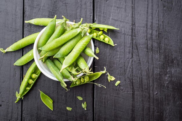 Une cosse de pois dans un bol sur le fond en bois noir