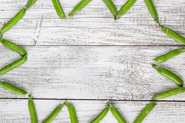 Cosses de pois verts sur une vue de dessus de table en bois blanc, espace de copie