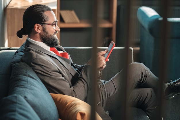 Costume cravate. Homme barbu portant un costume gris et une cravate rouge tenant son message de lecture de téléphone