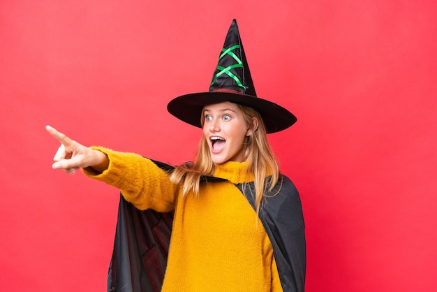 Costume de jeune femme caucasienne comme sorcière isolée sur fond rouge pointant vers l'extérieur