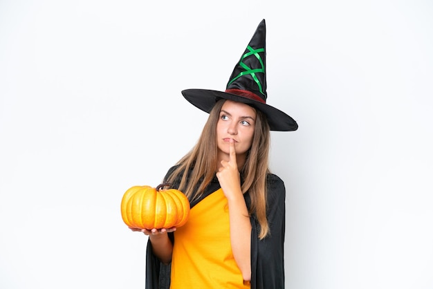 Costume de jeune femme caucasienne comme sorcière tenant une citrouille isolé sur fond blanc ayant des doutes tout en levant les yeux