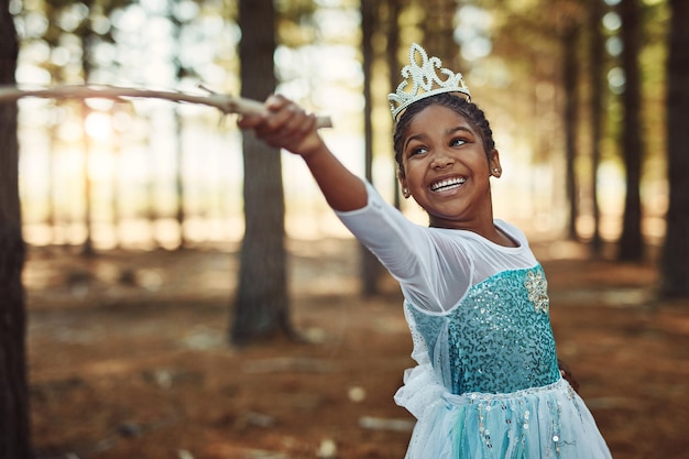 Costume de princesse de la forêt et fille avec bâton pour jouer à des jeux d'enfance fantastiques et bonheur Conte de fées de la nature et visage d'enfant heureux dans les bois jouent avec une branche pour l'aventure, la liberté et le plaisir