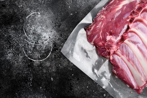 Côte d'agneau viande fraîche Ensemble scellé sous vide, sur fond de table en pierre noire noire, vue de dessus à plat, avec espace de copie pour le texte