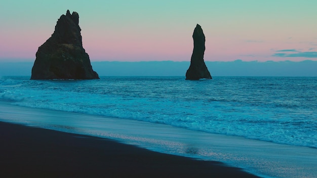 Côte atlantique avec des rochers majestueux sur la plage de reynisfjara et la montagne de reynisfjall, plages nordiques de sable noir. Paysage côtier islandais avec vagues océaniques, ciel rose. Tir à la main.