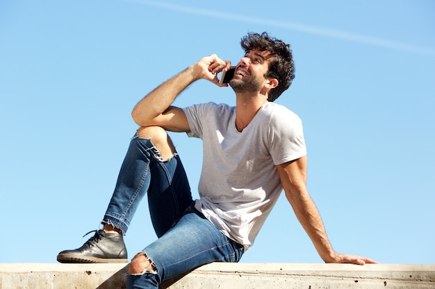 Côté d&#39;un homme heureux, assis sur un mur de béton, parler au téléphone intelligent