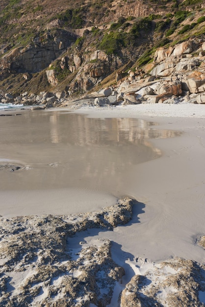 Une côte rocheuse sur une plage du Cap avec des montagnes en arrière-plan et un espace de copie Vue d'un rivage avec des rochers sur l'océan
