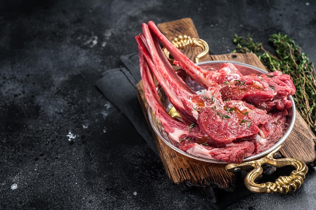 Côtelette de mouton d'agneau côtelette de viande crue dans une poêle avec des herbes Fond noir Vue de dessus Espace de copie