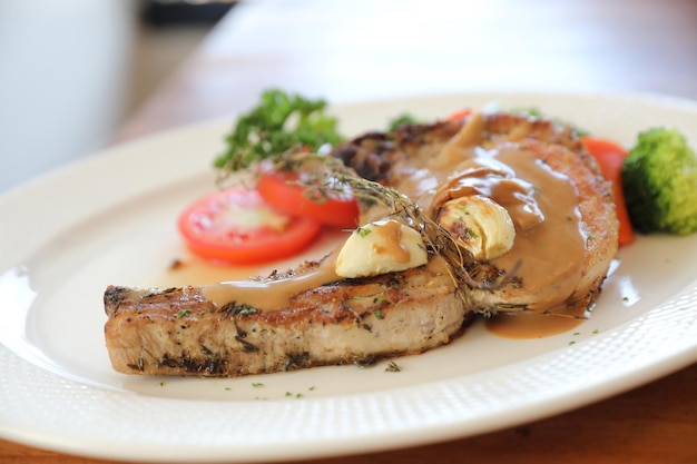 Côtelette de porc grillée avec légumes sur plat avec fond de table en bois