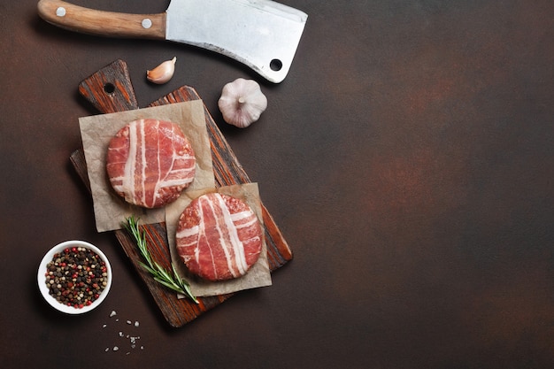 Côtelettes d'hamburger crues au romarin sur une planche à découper