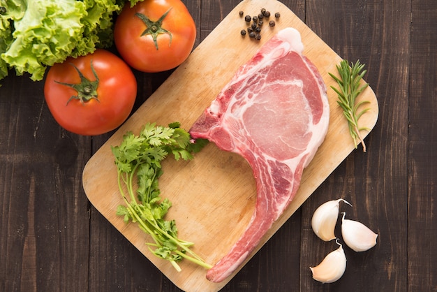 Photo côtelettes de porc crues fraîches et légumes sur bois