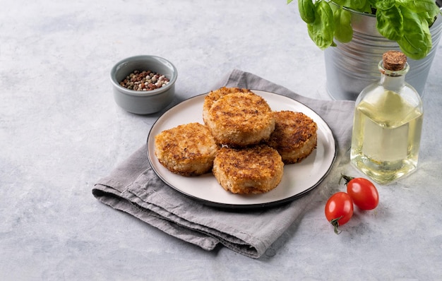 Des côtelettes de poulet frites sur une assiette sur un fond clair avec des herbes fraîches, de l'huile et des tomates.