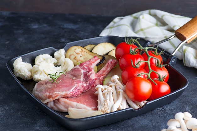 Côtes d'agneau crues marinées avec des légumes frais dans une poêle à frire sur une pierre sombre,