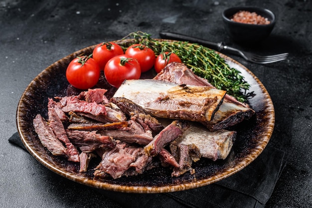 Côtes de bœuf fumées et grillées dans une assiette rustique aux herbes. Fond noir. Vue de dessus.