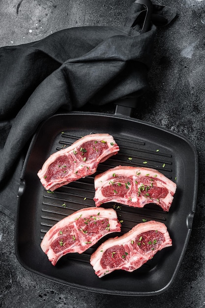 Côtes de côtes d'agneau crues steaks dans une poêle à griller avec du romarin et du thym Fond noir Vue de dessus