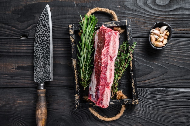 Côtes courtes de veau cru frais dans un plateau en bois avec des herbes