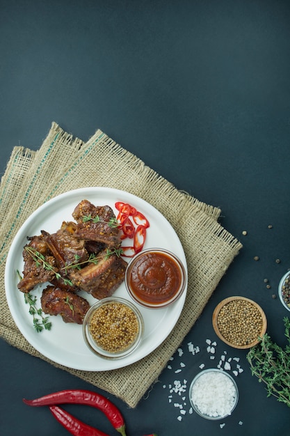 Côtes levées au four dans un plat blanc. Côtes de porc grillées aux épices et herbes fraîches. Fond sombre. Espace pour le texte. Menu d'arrière-plan du tableau.