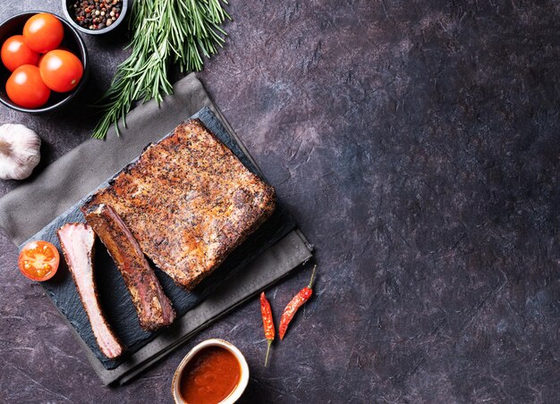 Côtes levées de porc barbecue juteuses avec sauce tomate et herbes fraîches sur fond sombre