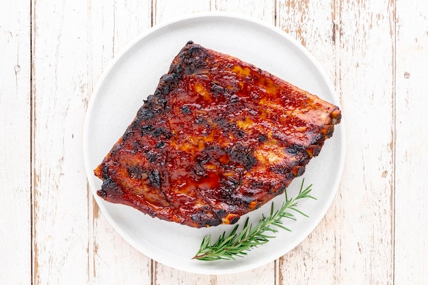 Photo côtes levées de porc rôties au barbecue avec de l'origan au miel et du romarin dans une assiette en céramique simplement blanche sur un vieux fond de texture de bois blanc vue de dessus à plat