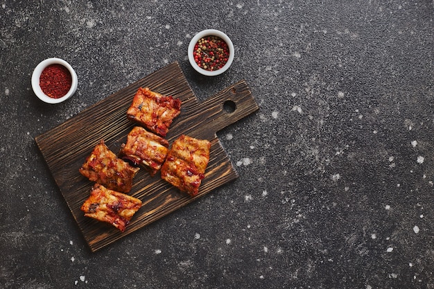 Côtes de porc au four appétissantes avec du poivre et du paprika sur une planche à découper en bois sur fond sombre americ...