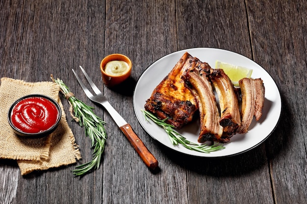 Côtes de porc grillées au citron et au romarin sur une assiette sur une table en bois sombre avec du ketchup et de la moutarde vue horizontale d'en haut