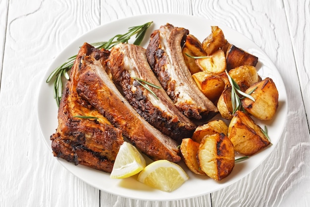 Côtes de porc grillées servies avec des pommes de terre nouvelles rôties sur une plaque blanche sur une table en bois vue horizontale d'en haut