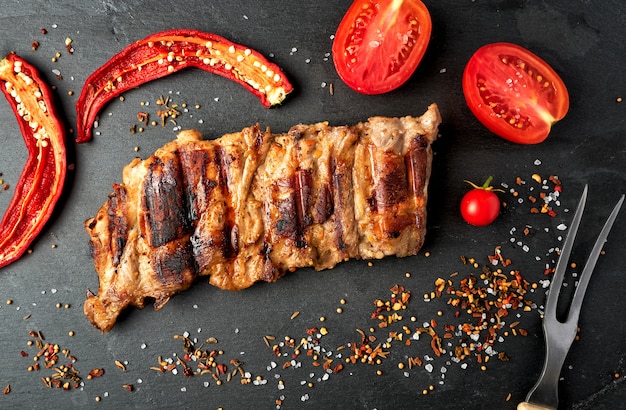 Côtes de porc grillées sur un tableau noir, tomates rouges fraîches