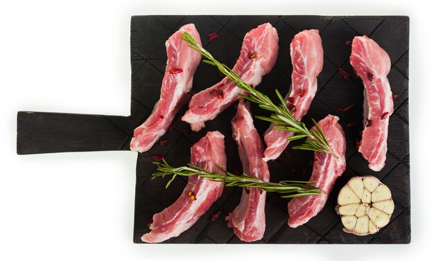 Côtes de porc hachées crues au romarin et à l'ail sur une planche sombre, isoler