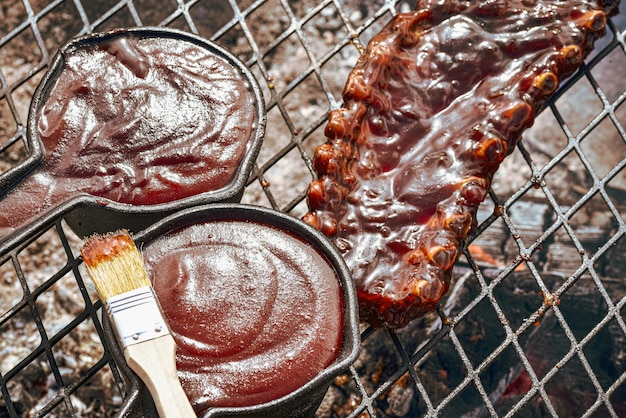 Photo des côtes de porc et des pots en fonte remplis de sauce barbecue sur le gril.