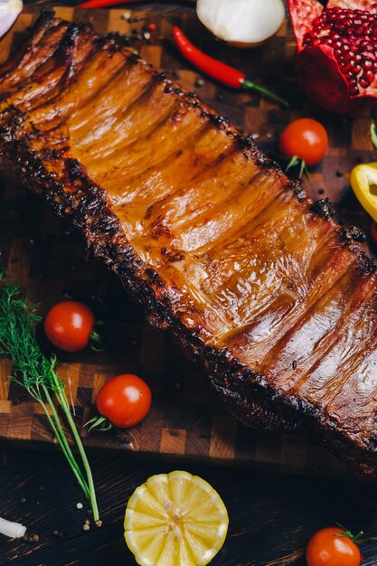 Photo côtes de porc rôties dans un fumoir debout sur une planche à couper garnies de romarin poivre piment poivre tomate citron grenade viande cuite aromatique