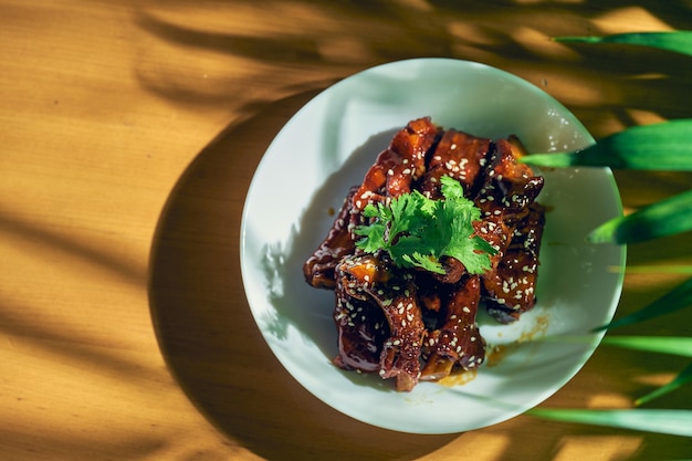 Côtes de porc à la sauce aigre-douce avec coriandre, graines de sésame et poivre du Sichuan dans un bol blanc. cuisine chinoise