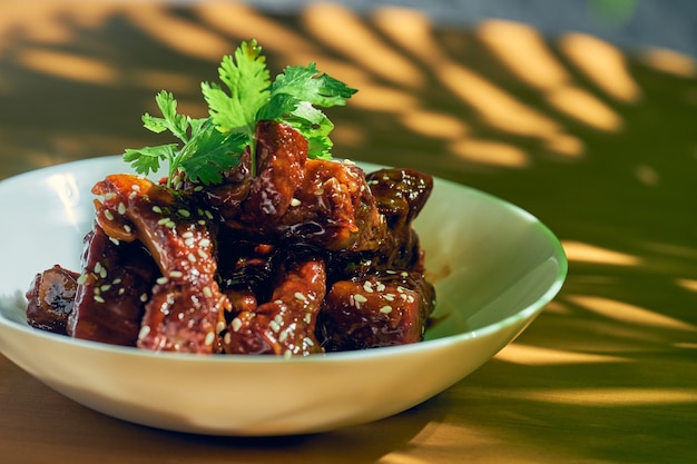 Côtes de porc à la sauce aigre-douce avec coriandre, graines de sésame et poivre du Sichuan dans un bol blanc. cuisine chinoise