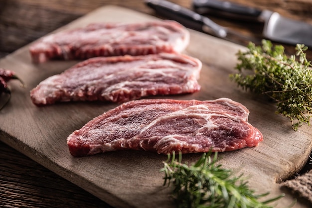 Cou de porc cru coupé sur une planche à découper avec des herbes de romarin et de thym