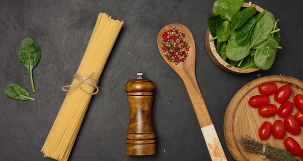 Une couche plate d'épinards frais, de tomates cerises, de spaghettis et d'épices sur une surface rustique sombre